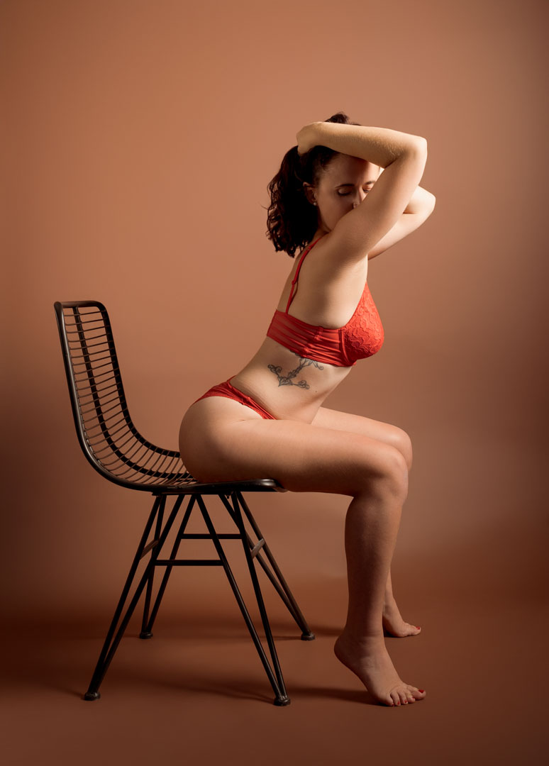 Femme en lingerie rouge posant sur une chaise lors d'une séance photo en studio à Berck